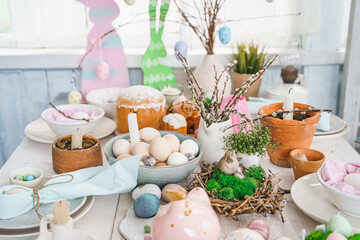 Table decoration for Easter celebration in kitchen.Tablescape for Easter holiday at home.Family religious traditional festive christianity,catholic meal food.Pop color eggs,cake,fun bunny,candy sweet