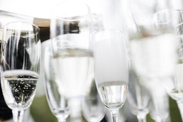 Bartender pouring champagne or wine into wine glasses on the table at the outdoors solemn wedding ceremony. 