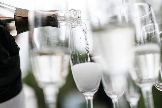 Bartender pouring champagne or wine into wine glasses on the table at the outdoors solemn wedding ceremony. 