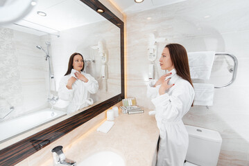 A young beautiful girl washes her face and holds a towel in a beautiful white bathroom. A fresh good morning at the hotel. Rest and travel. Hotel recreation, and tourism.