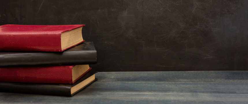 Back to school. Book stack on blue wood, blank empty blackboard background, copy space