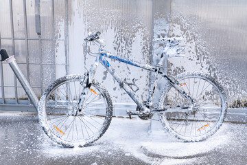 Washing a bicycle with a foam jet at a car wash. The bike is covered with foam. Self-service....