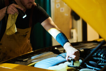 Hand of young mechanic in workwear fixing part of car engine while bending over it and directing...