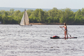 Naklejka premium Men, friends ride SUP boards on a big river during sunrise.