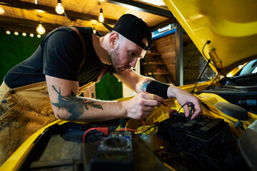 Young repairman bending over open hood with engine during technical checkup or diagnostics of car...