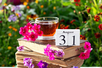 August 31. Cup of tea and calendar date on stack of books against bright floral background, summer...