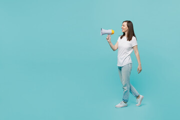 Full body side view young fun caucasian woman 20s she wear white t-shirt walk go hold scream in megaphone announces discounts sale Hurry up isolated on plain pastel light blue cyan background studio.