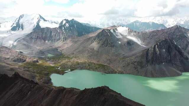 Man in red stay on edge of cliff. Ala-Kul Lake in Issyk Kul Region in Kyrgyzstan. Drone footage 4K. Mountains with big lake and epic clouds. 