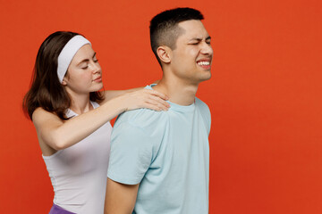 Young fitness trainer instructor sporty two man woman in headband t-shirt massaging neck suffer from pain spend weekend in home gym isolated on plain orange background Workout sport lifestyle concept.