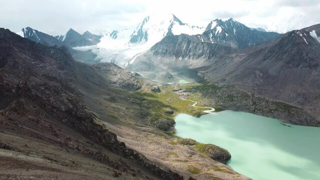 Man in red stay on edge of cliff. Ala-Kul Lake in Issyk Kul Region in Kyrgyzstan. Drone footage 4K. Mountains with big lake and epic clouds. 