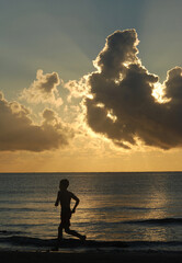 The silhouette of a young boy running along the seashore at dawn against a cloudy tropical sky