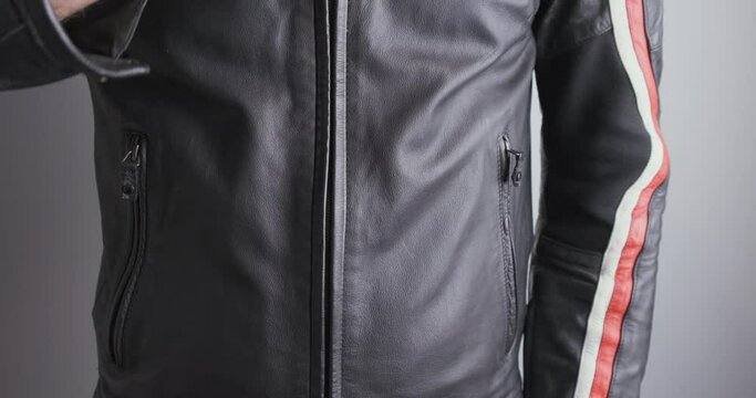 Motorcyclist unzip black moto jacket. Close-up, front view of the chest, indoors. Concept of protection when riding a motorcycle, preparing for a trip.