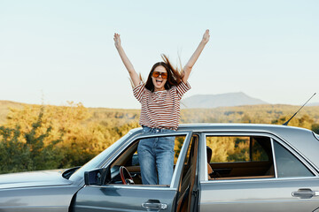 Happy woman traveler climbed on the car and spread her arms smiling happily. looks at the nature around. Lifestyle in travel and joy