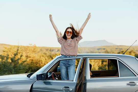 Happy woman traveler climbed on the car and spread her arms smiling happily. looks at the nature around. Lifestyle in travel and joy
