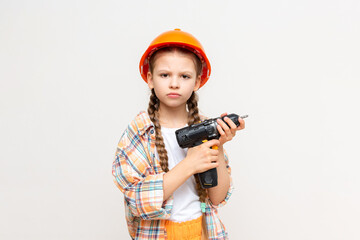 A little girl with a drill and wearing a protective construction helmet depicts a builder on a...