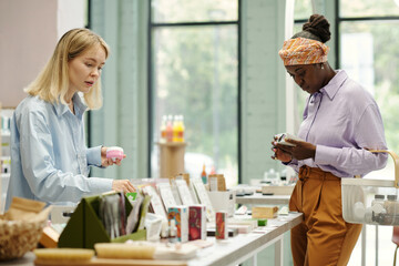 Two young female customers choosing makeup products such as face cream, masks, patches, nail polishers and others on discount display