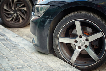 .Car wheel parked close to the curb on parking lot. 225/40r18 tire and bumper with scratch. Front...