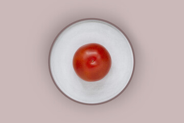 Red tomato in a white plate on a beige background, top view.