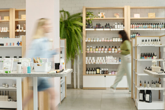 Blurry motion of two young women moving along displays with self care items such as bodycare, skincare, nailcare and makeup products