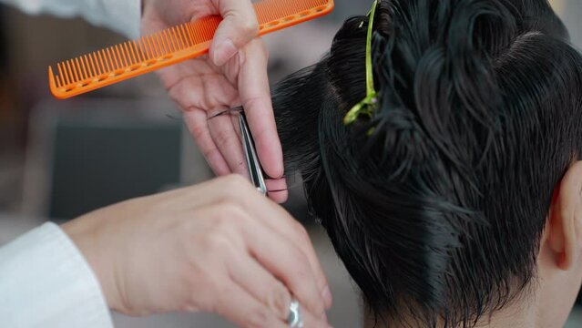 Asian professional male using scissors cutting customer hair in salon. Attractive hairdresser man using scissors cut hair young men and looking at mirror with smiling. Beauty salon business concept.