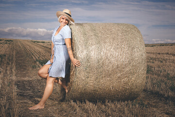Naklejka na ściany i meble Pretty lady in summer apparel posing on harvested cornfield