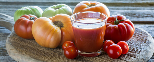 Narrow view of a glass of tomato juice surrounded by a variety of tomatoes.