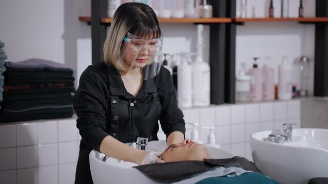 Asian attractive young male get hair washed by hairdresser in salon. Professional hair stylist woman give service and hair wash and massage to handsome man customer lying down on salon washing bed.