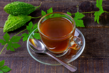 Bitter gourd or bitter melon tea in transparent cup and fresh bitter gourd with green leaf on rustic wooden table. Scientific name is Momordica charantia. 