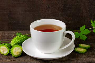 Bitter gourd or bitter melon tea in ceramic cup with fresh bitter gourd and green leaf on rustic wooden table. Scientific name is Momordica charantia. As a whole food and herbs for treating diseases.