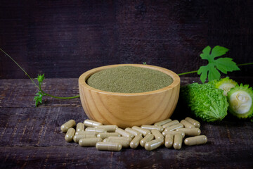 Bitter gourd or bitter melon powder on wooden bowl with fresh bitter gourd and green leaf on rustic wooden table. Scientific name is Momordica charantia. 