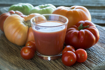 A glass of tomato juice surrounded by tomatoes of different shapes and sizes.