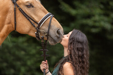 A female equestrian cuddles with her bridled kinsky horse. Portrait of a young woman giving a...