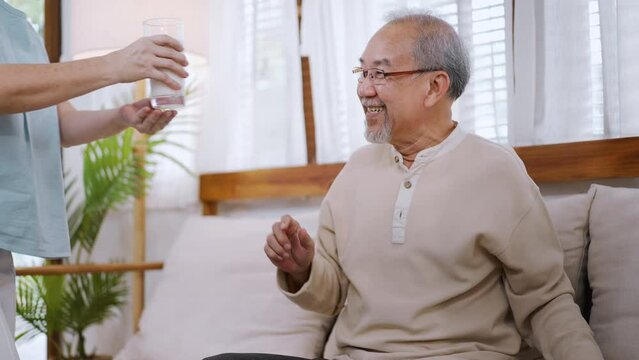 Asian senior elderly couple spend time together enjoy retirement life. Attractive older grandmother serving a cup of milk to grandfather in living room. Relationship and health care in house concept.