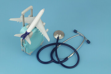 Airplane on travel suitcase and stethoscope on blue background. Travel insurance and medical...