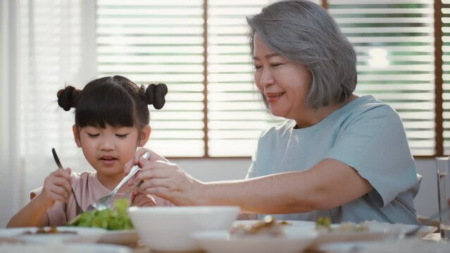 Big Asian happy family spend time having lunch on dinner table together. little kid daughter enjoy eating food with father, mother and grandparents. Multi-Generation relationship and activity in house