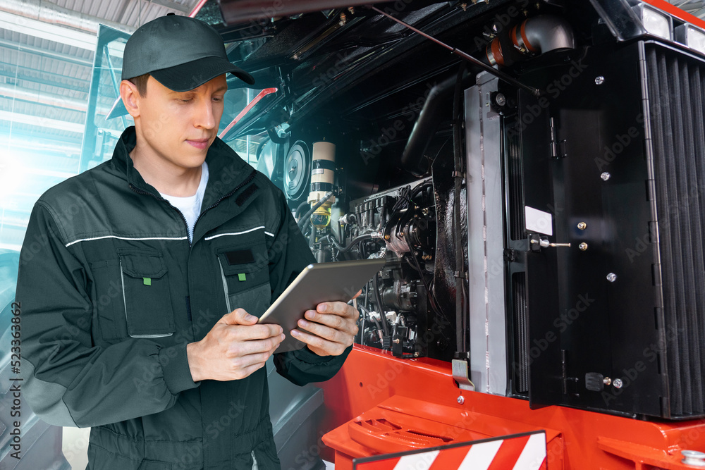 Poster Serviceman with digital tablet on a background of the tractor with open hood