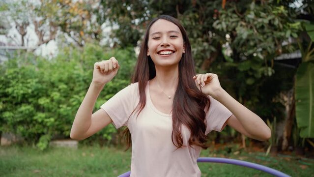 Asian beautiful young woman doing cardio workout in garden at house. Happy attractive girl enjoy free leisure activity exercise rotating hula hoop to lose weight for healthcare and well being at home.