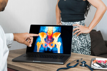 Doctor showing a x-ray of pain in the hips on a laptop. Woman patient in the background