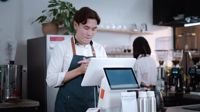Asian cafe business male owner checking report sales on computer laptop. Handsome barista worker check process order on counter bar in restaurant with feel glad and success for income at coffee shop.