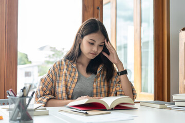Young woman student is suffering serious tiredness and headaches while reading hard textbook