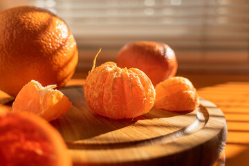 Peeled orange tangerine on a wooden plank on an orange wooden window sill in oblique rays of sunlight through the blinds, lines of light and shadow on the orange window sill surface - Powered by Adobe