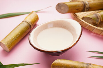 Fresh sugar cane juice and sugar cane on a pink background. Closeup.