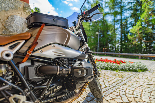 Closeup motorcycle parked on driveway road in warm sunny light. Blurred forest trees, park flowers and gravel stone road. Classic vintage motorbike, outdoor sport recreational pursuit. Nature travel