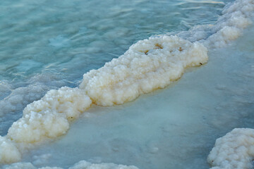 Fototapeta premium Natural sea-salt beach, seashore background. Texture of Dead sea coastline. Salt crystals at sunset, close up. Salty sea shore. Organic salt crystal on the Dead Sea shore. Travel Photos of Israel.