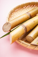 Sugar cane and green leaf in a wooden tray on a pink background, vertically.
