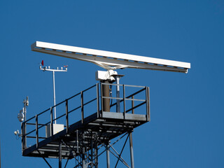 A rotating antenna in white on a blue sky background in bright daylight