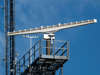 A rotating antenna in white on a blue sky background in bright daylight