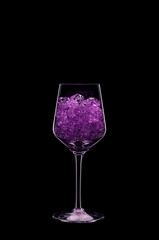 Wine glass filled with transparent violet crystals backlit and isolated on black background. Beverage glassware concept. Copy space.