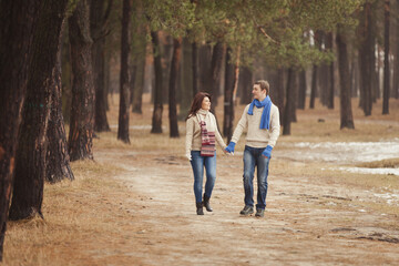 Fototapeta premium couple on a date walk in autumn or winter park. Valentine's Day for couple in rustic style. Happy couple in love. Casual outfit with Blue accessories: scarfs and mittens. Cozy winter in Pine forest