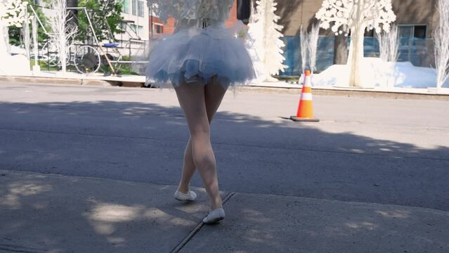 Short movie in slow mo on the bare legs of a dance street entertainer, wearing white frilly short skirt and ballet shoes on a sidewalk in Montreal.